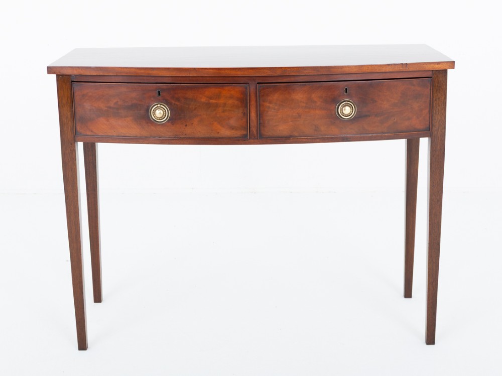A Regency mahogany bow-front side table featuring two drawers with brass ring handles and slender square tapered legs. View VI
