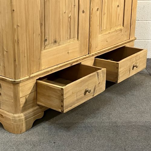 fig 3. A large Victorian pine double wardrobe featuring fielded panel doors, iron escutcheons, and two base drawers on a plinth foundation.