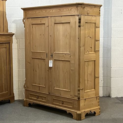 fig 1. A large antique pine double wardrobe featuring panelled doors, two bottom drawers with turned handles, and a moulded top cornice.