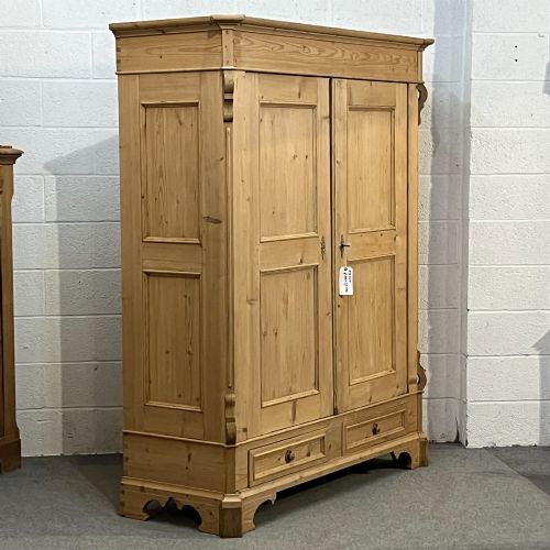 fig 2. A large antique pine double wardrobe featuring panelled doors, two bottom drawers with turned handles, and a moulded top cornice.