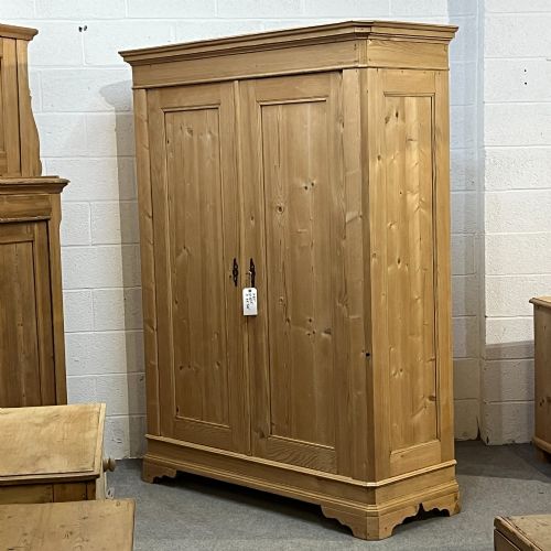 fig 2. A large two-door antique pine wardrobe with fielded panels, a plain stepped cornice, moulding at the base, and central iron escutcheons.