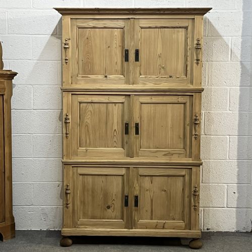 fig 1. A three-section antique pine campaign cupboard featuring panelled doors, iron carrying handles on the sides, and rounded bun feet.