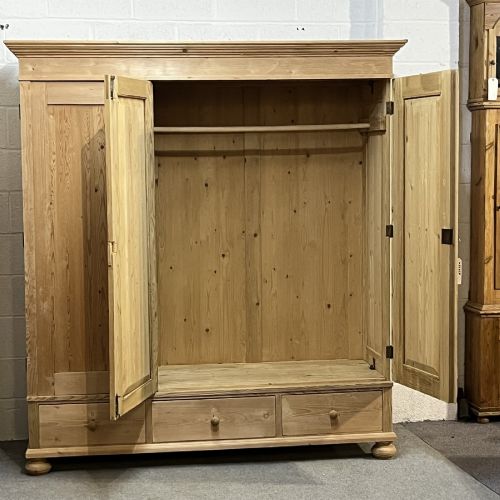 fig 1. A large natural pine triple wardrobe featuring three vertical panelled doors above three aligned base drawers with turned wooden knobs.