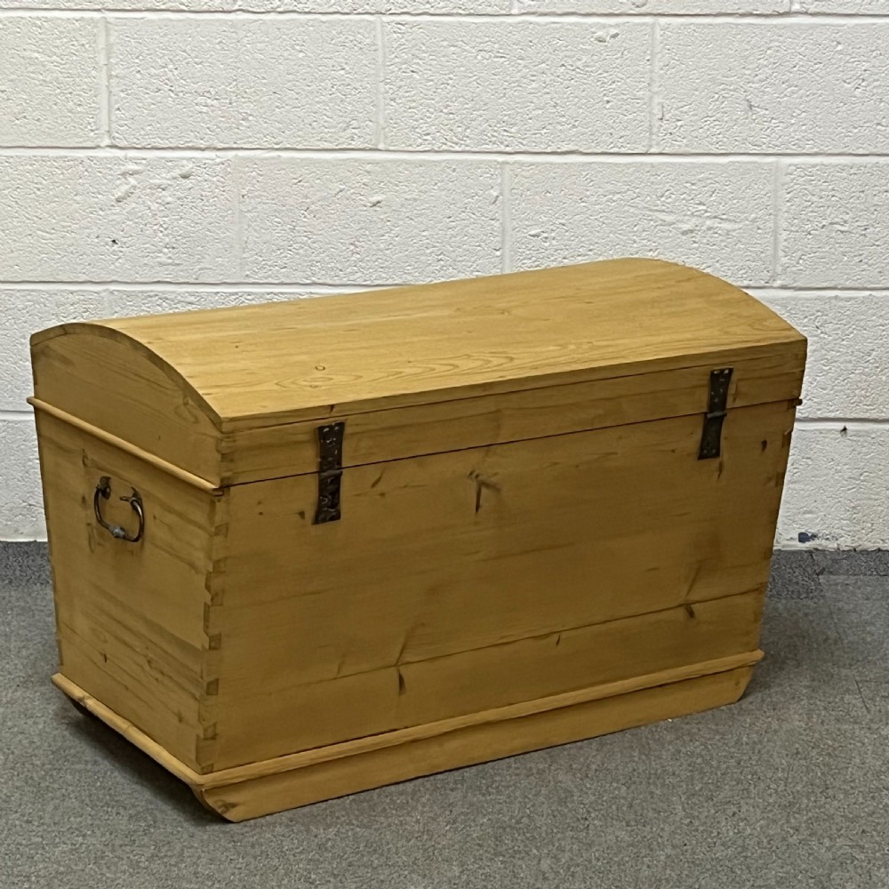 A solid honey-toned pine dome top trunk with visible corner dovetail joints, metal side carrying handles, and a central keyhole escutcheon. View III