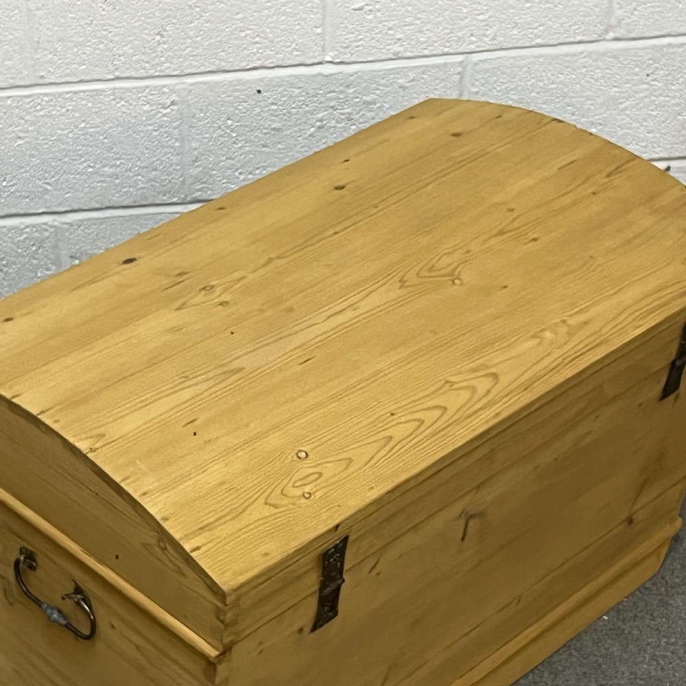 A solid honey-toned pine dome top trunk with visible corner dovetail joints, metal side carrying handles, and a central keyhole escutcheon. View IV