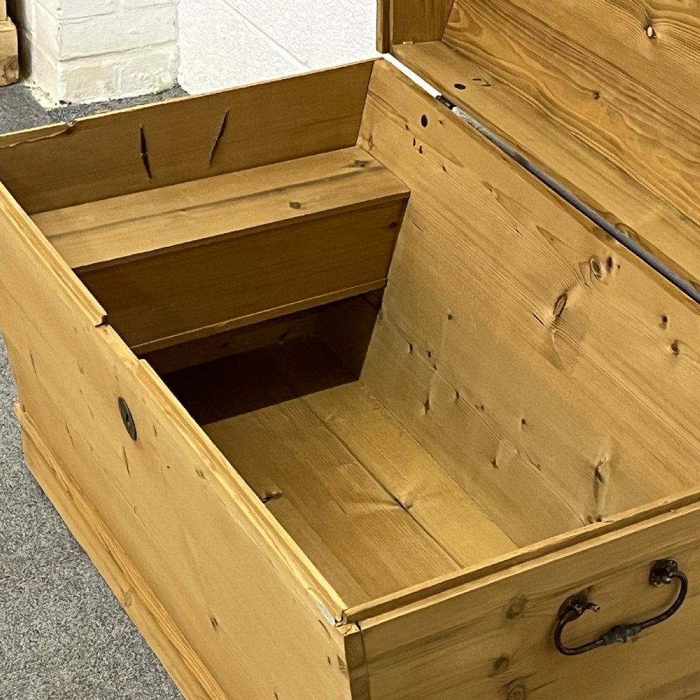 A solid honey-toned pine dome top trunk with visible corner dovetail joints, metal side carrying handles, and a central keyhole escutcheon. View VII