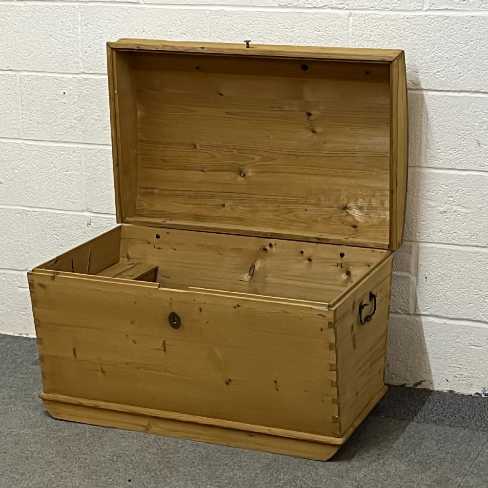 A solid honey-toned pine dome top trunk with visible corner dovetail joints, metal side carrying handles, and a central keyhole escutcheon. View VIII