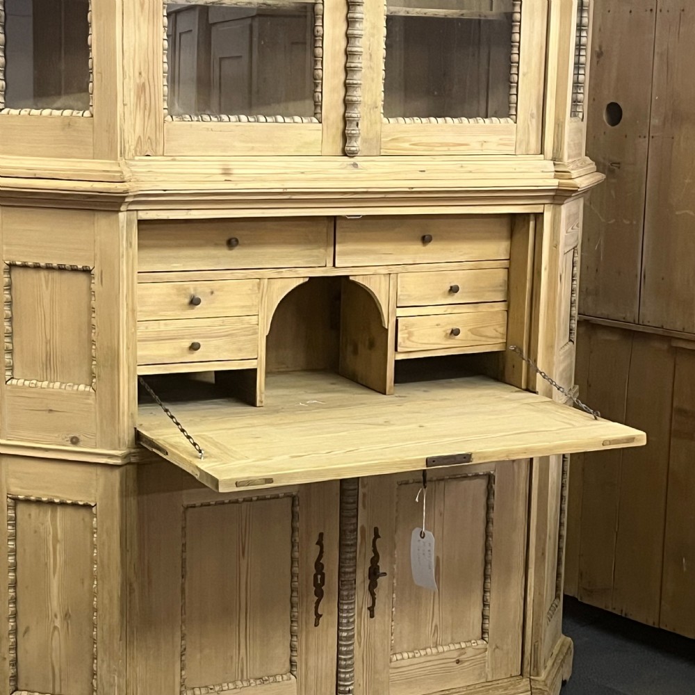 A large natural pine secretaire bookcase featuring glazed upper doors, a fold-down desk surface with internal drawers, and a lower two-door cupboard. View III