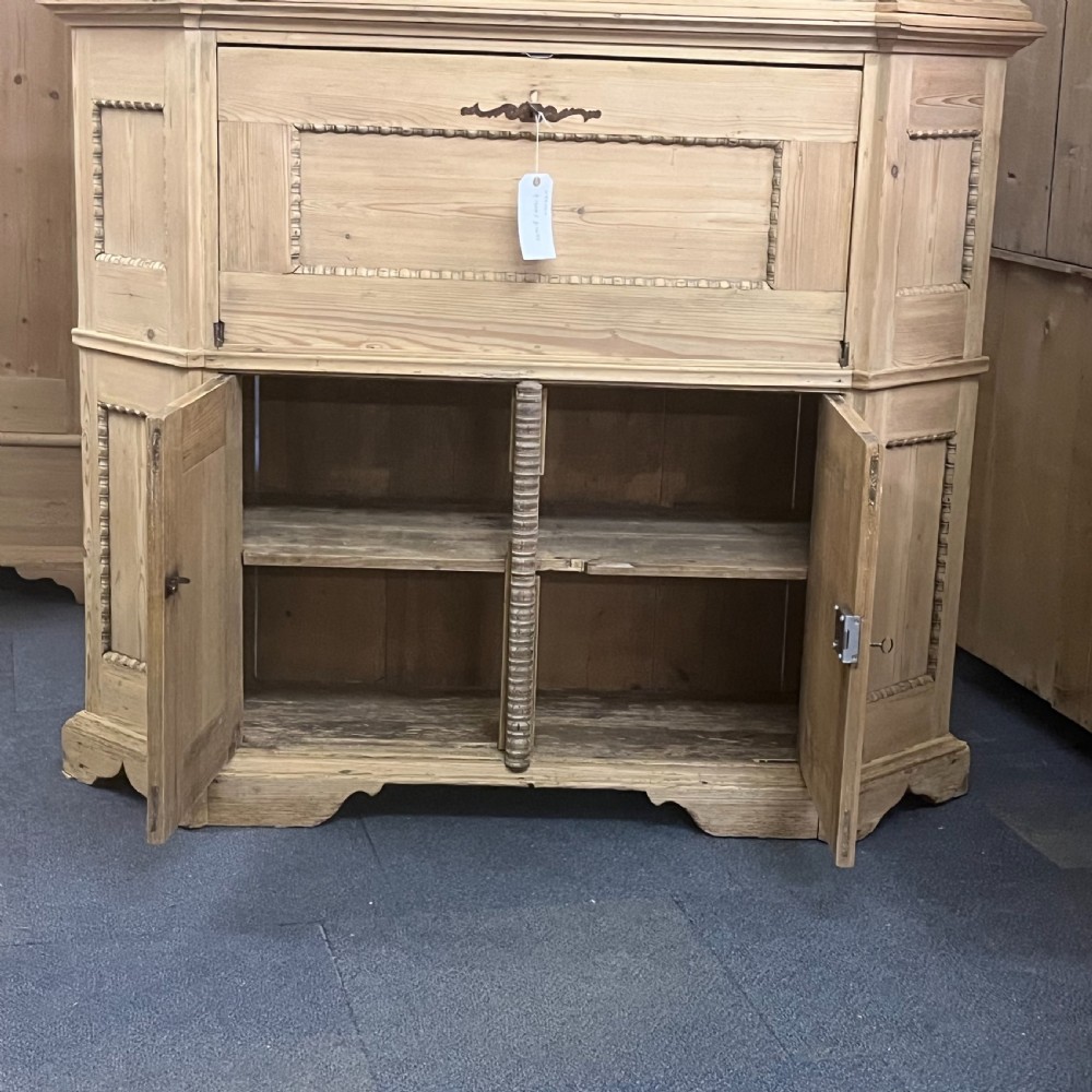 A large natural pine secretaire bookcase featuring glazed upper doors, a fold-down desk surface with internal drawers, and a lower two-door cupboard. View X