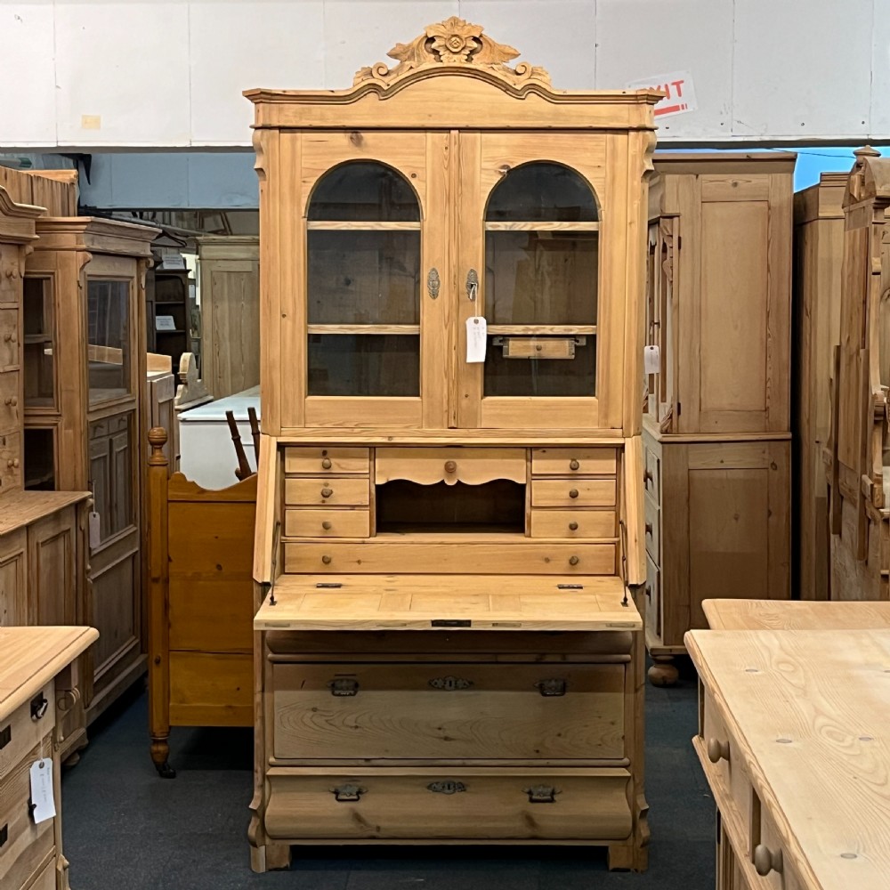 A tall antique pine secretaire bookcase featuring an upper glazed cabinet with arched doors, a fall-front writing surface, and a lower chest of drawers with decorative handles. View II