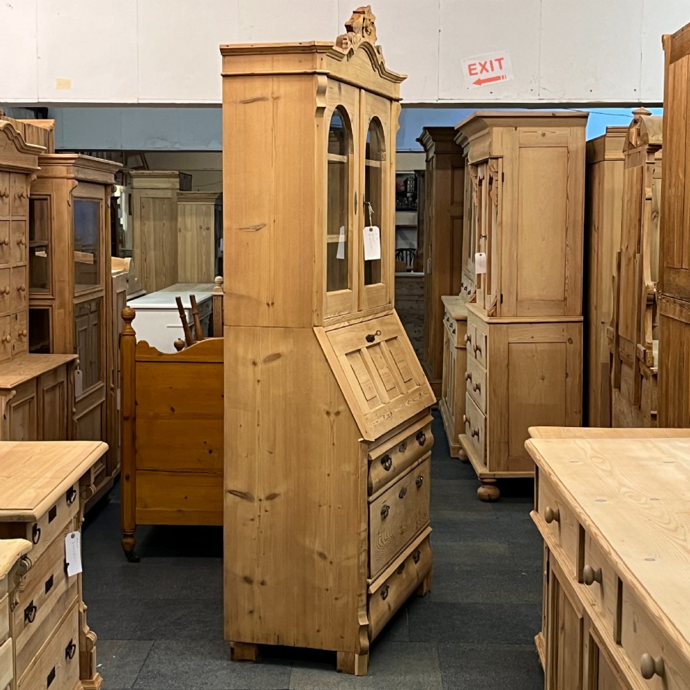A tall antique pine secretaire bookcase featuring an upper glazed cabinet with arched doors, a fall-front writing surface, and a lower chest of drawers with decorative handles. View V