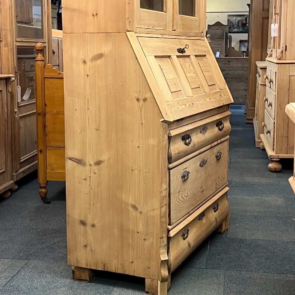 A tall antique pine secretaire bookcase featuring an upper glazed cabinet with arched doors, a fall-front writing surface, and a lower chest of drawers with decorative handles. View VII