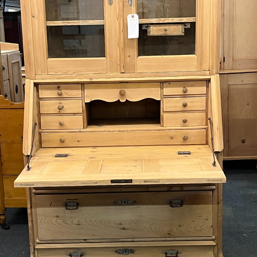 A tall antique pine secretaire bookcase featuring an upper glazed cabinet with arched doors, a fall-front writing surface, and a lower chest of drawers with decorative handles. View VIII