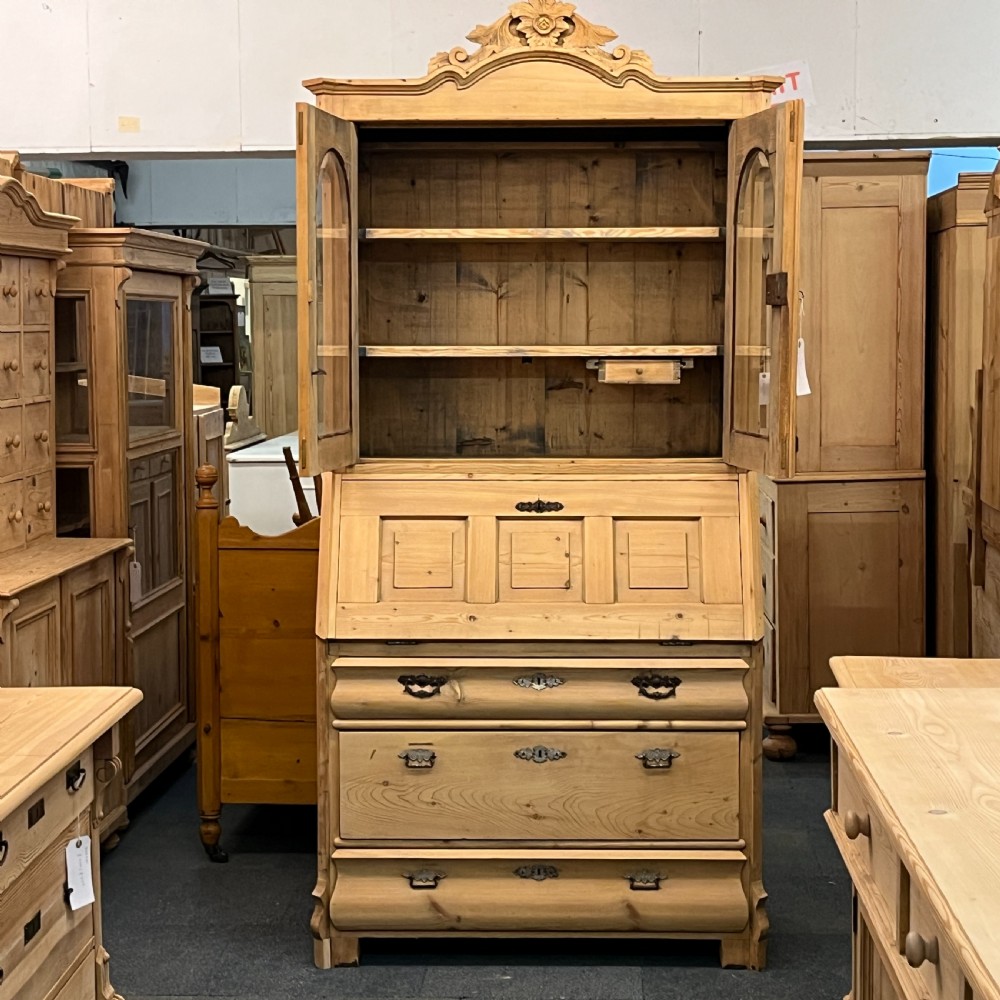 A tall antique pine secretaire bookcase featuring an upper glazed cabinet with arched doors, a fall-front writing surface, and a lower chest of drawers with decorative handles. View IX