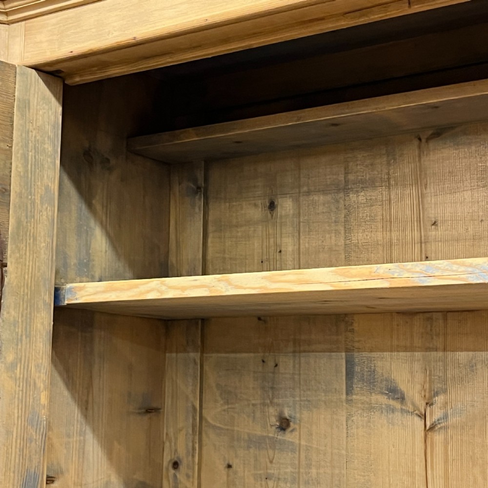 A tall antique pine secretaire bookcase featuring an upper glazed cabinet with arched doors, a fall-front writing surface, and a lower chest of drawers with decorative handles. View XI