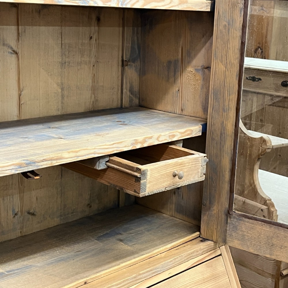 A tall antique pine secretaire bookcase featuring an upper glazed cabinet with arched doors, a fall-front writing surface, and a lower chest of drawers with decorative handles. View XII