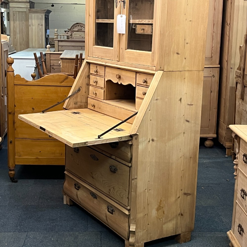 A tall antique pine secretaire bookcase featuring an upper glazed cabinet with arched doors, a fall-front writing surface, and a lower chest of drawers with decorative handles. View XIII