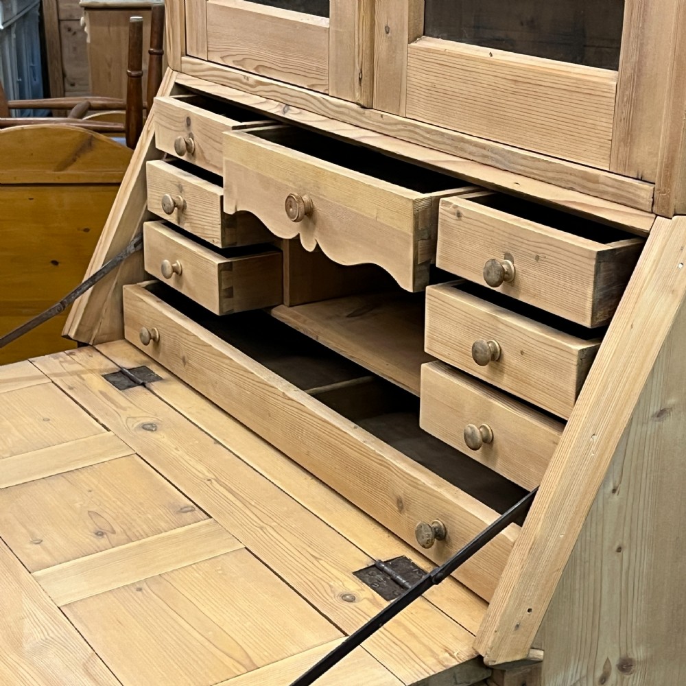 A tall antique pine secretaire bookcase featuring an upper glazed cabinet with arched doors, a fall-front writing surface, and a lower chest of drawers with decorative handles. View XIV