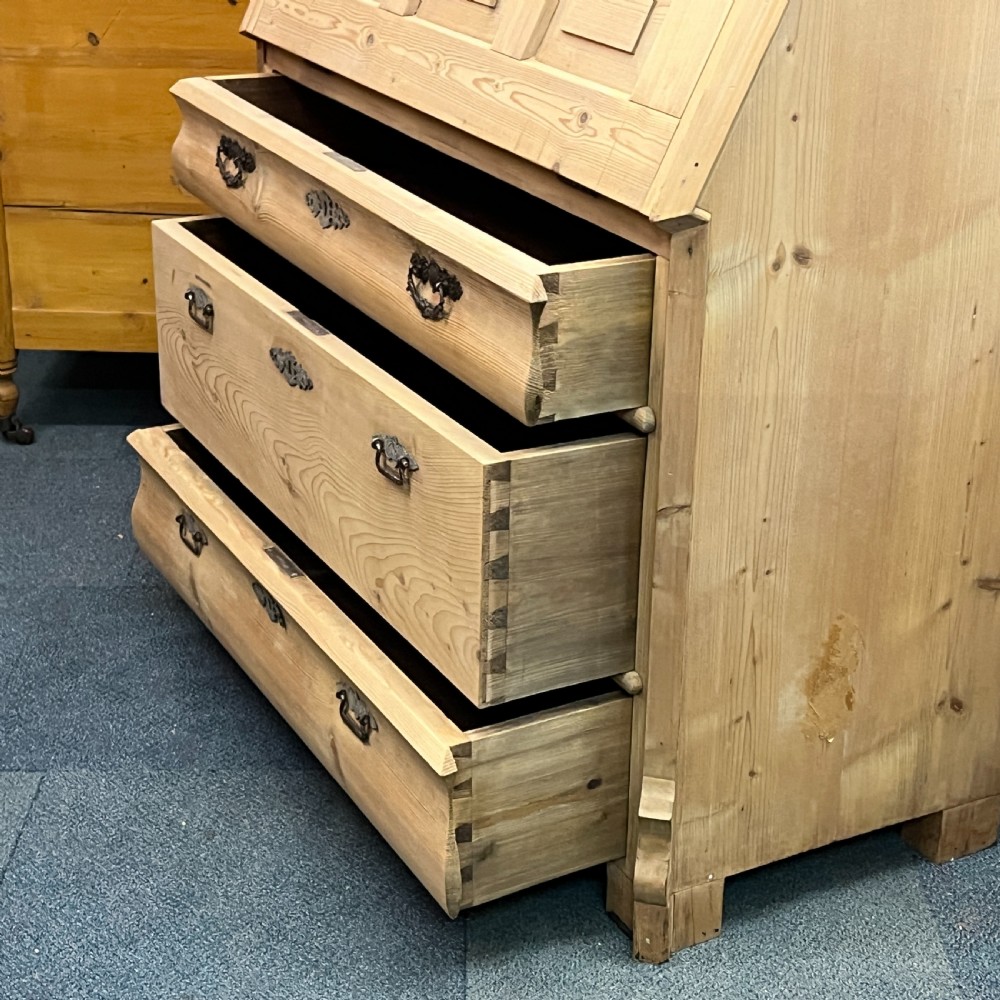 A tall antique pine secretaire bookcase featuring an upper glazed cabinet with arched doors, a fall-front writing surface, and a lower chest of drawers with decorative handles. View XV