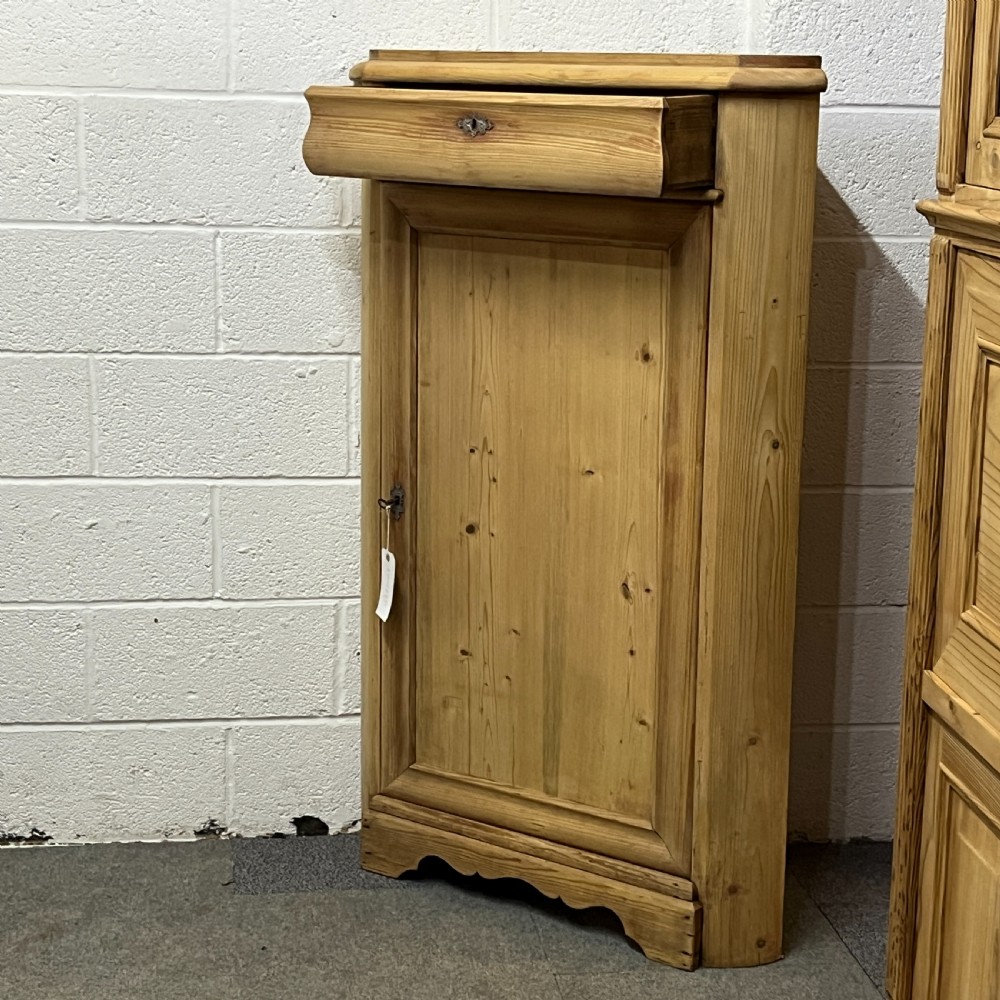A natural stripped pine freestanding corner cupboard featuring a top drawer, a single panel door with keyhole escutcheon, and a shaped apron base. View III