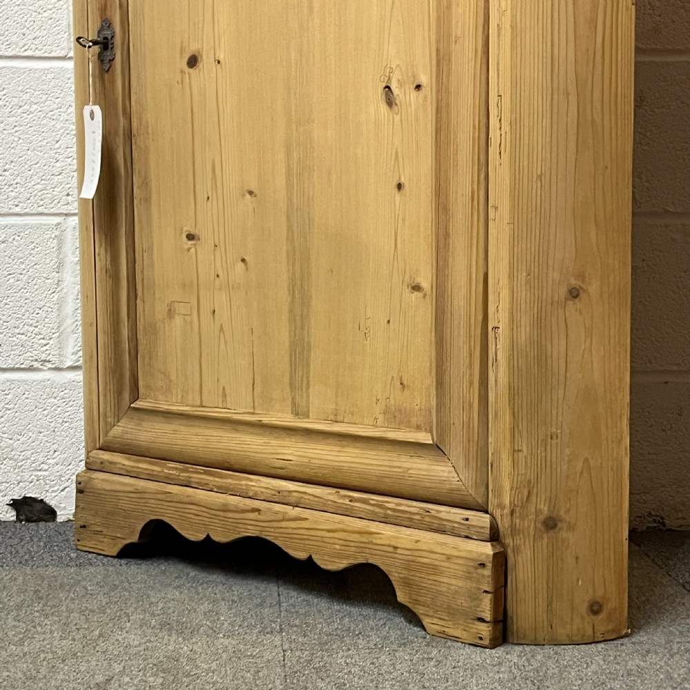A natural stripped pine freestanding corner cupboard featuring a top drawer, a single panel door with keyhole escutcheon, and a shaped apron base. View VII