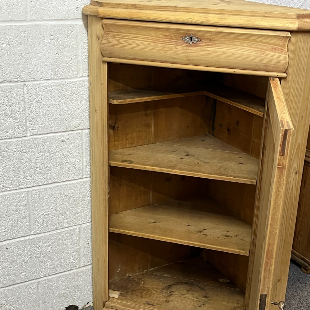 A natural stripped pine freestanding corner cupboard featuring a top drawer, a single panel door with keyhole escutcheon, and a shaped apron base. View IX