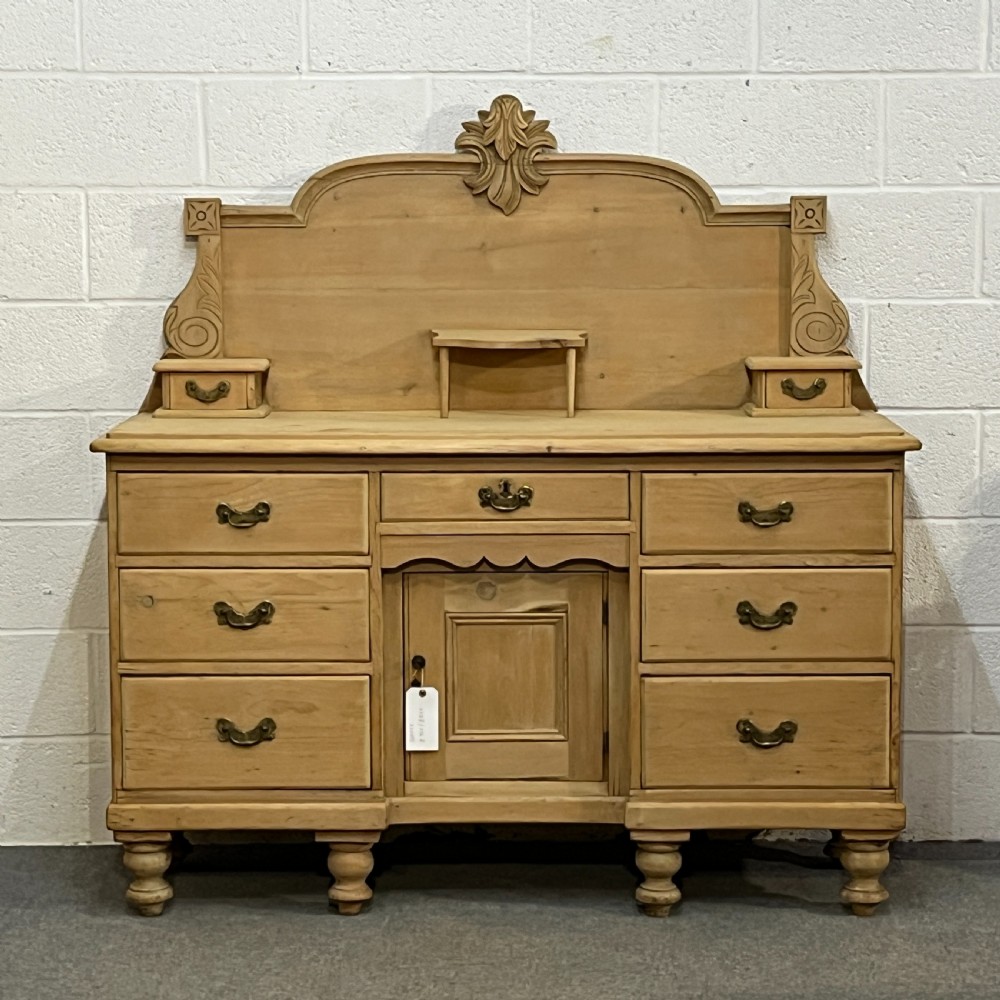 A Victorian stripped pine chiffonier sideboard featuring a decorative raised gallery back with a carved crest, small drawers, a central cupboard, and turned bun feet.