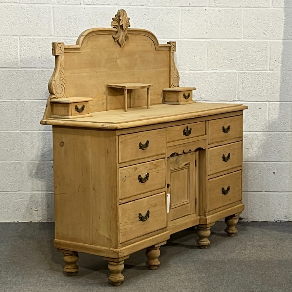 A Victorian stripped pine chiffonier sideboard featuring a decorative raised gallery back with a carved crest, small drawers, a central cupboard, and turned bun feet. View II