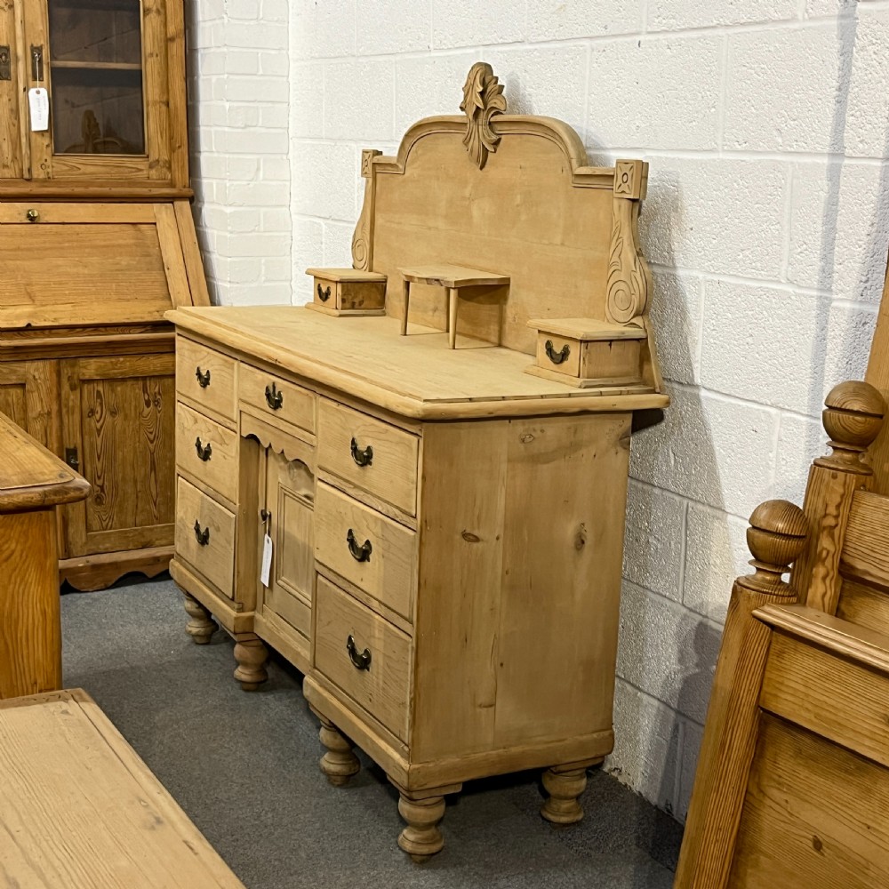 A Victorian stripped pine chiffonier sideboard featuring a decorative raised gallery back with a carved crest, small drawers, a central cupboard, and turned bun feet. View III