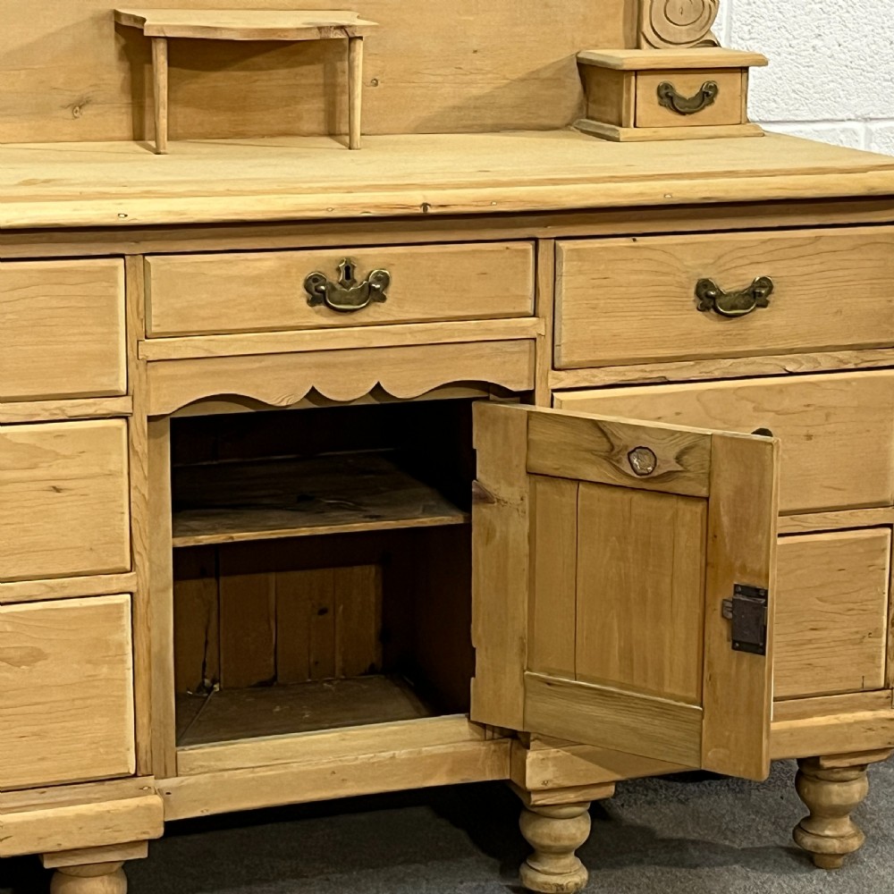 A Victorian stripped pine chiffonier sideboard featuring a decorative raised gallery back with a carved crest, small drawers, a central cupboard, and turned bun feet. View IV
