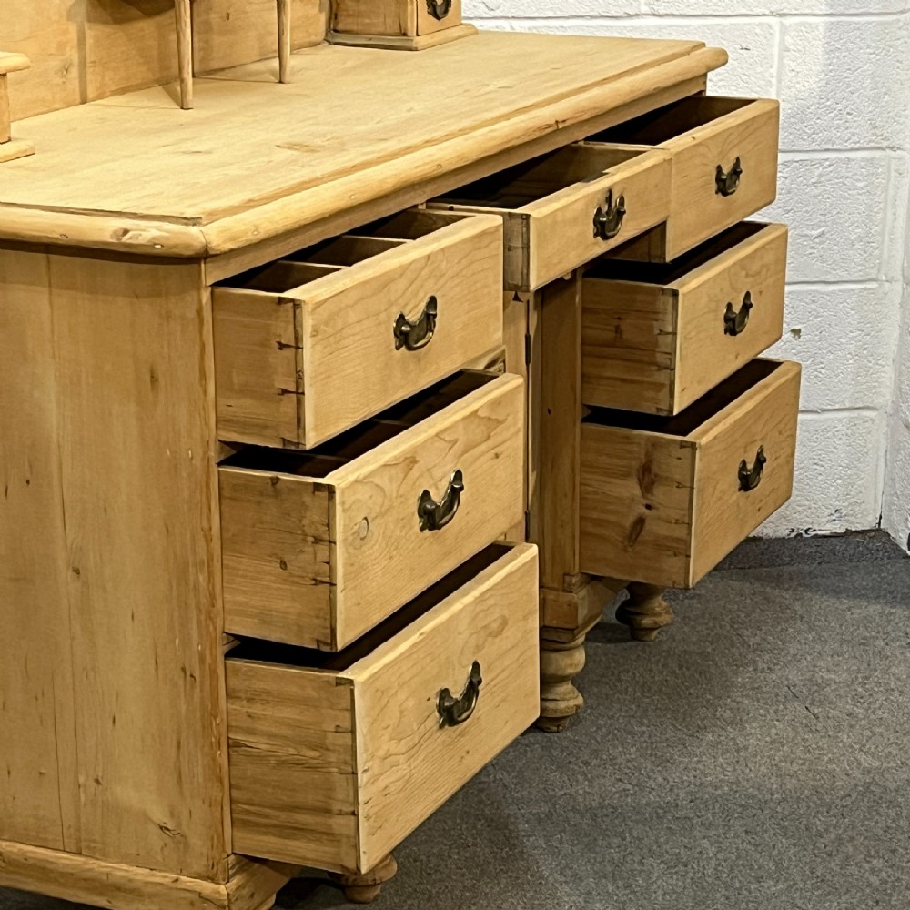 A Victorian stripped pine chiffonier sideboard featuring a decorative raised gallery back with a carved crest, small drawers, a central cupboard, and turned bun feet. View V