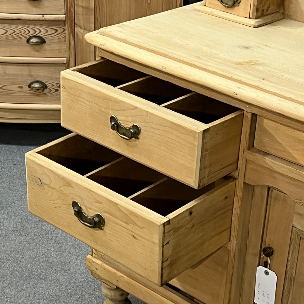 A Victorian stripped pine chiffonier sideboard featuring a decorative raised gallery back with a carved crest, small drawers, a central cupboard, and turned bun feet. View VII