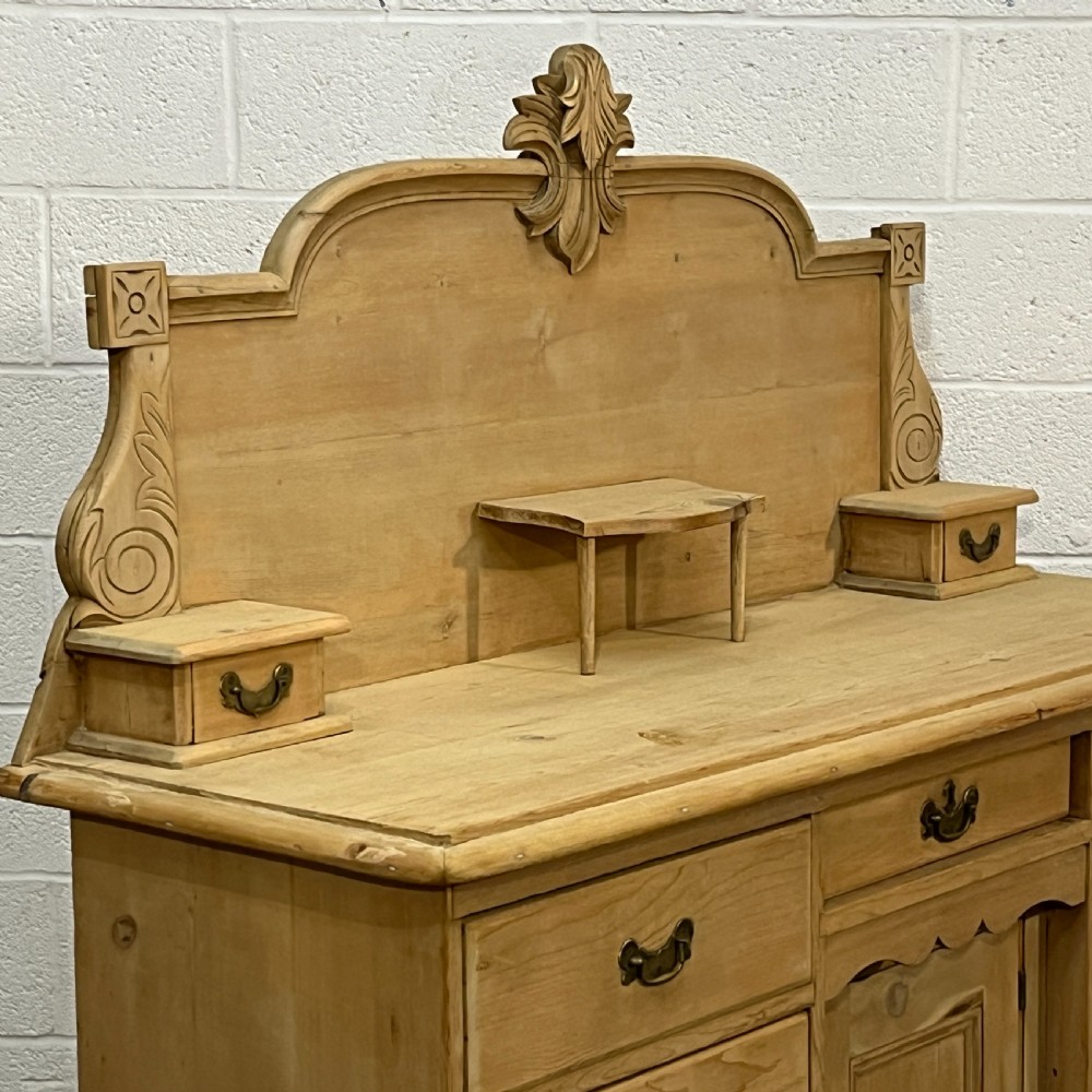 A Victorian stripped pine chiffonier sideboard featuring a decorative raised gallery back with a carved crest, small drawers, a central cupboard, and turned bun feet. View IX