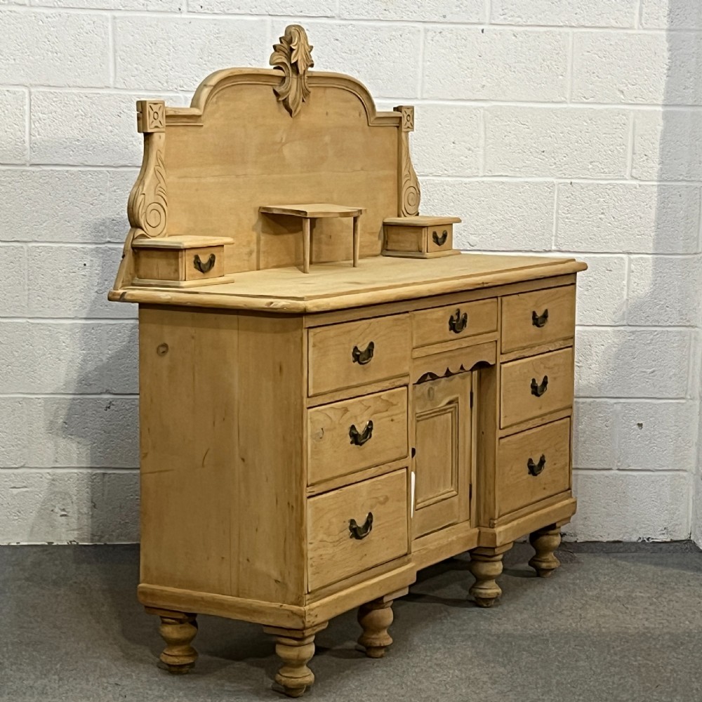 A Victorian stripped pine chiffonier sideboard featuring a decorative raised gallery back with a carved crest, small drawers, a central cupboard, and turned bun feet. View X