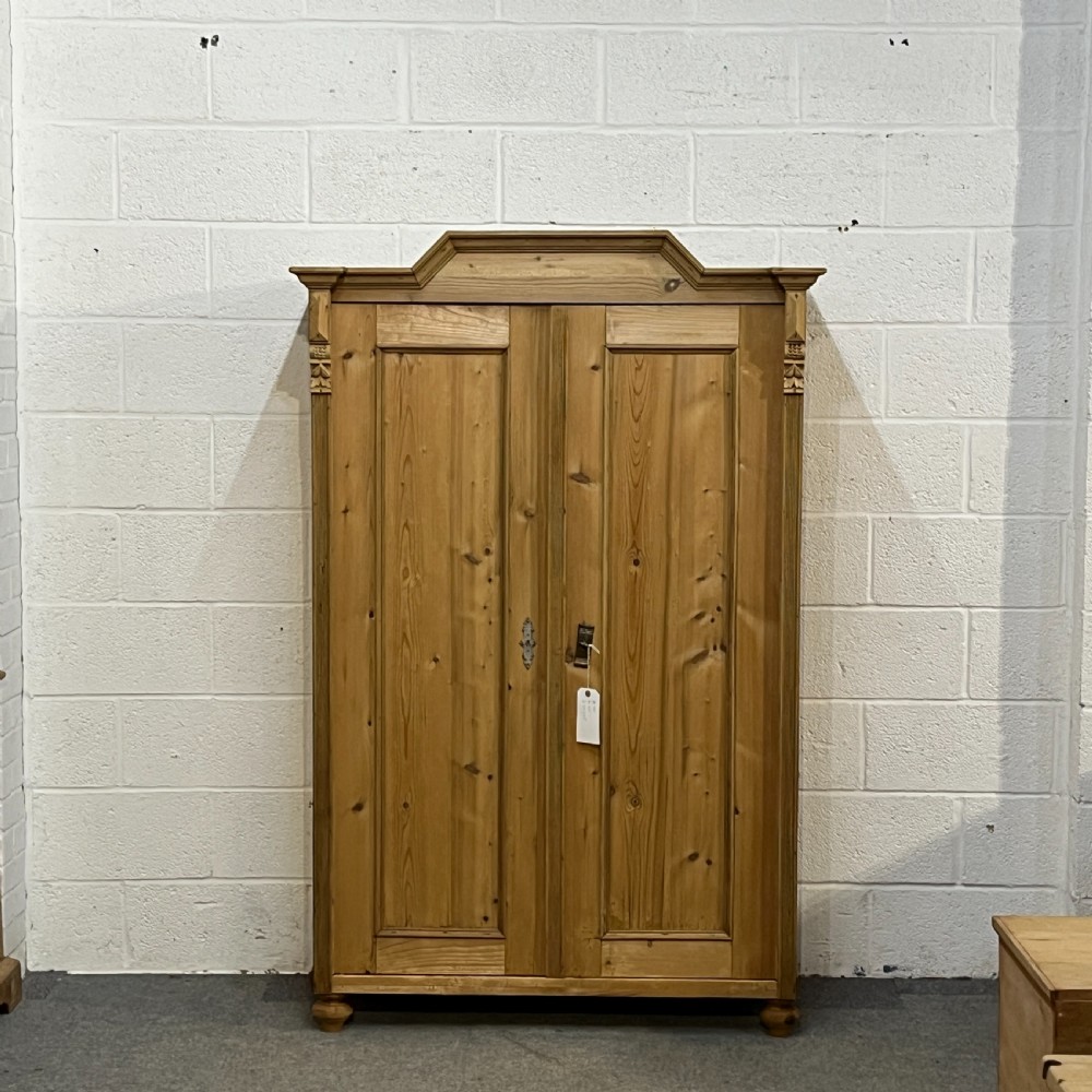 A tall Victorian pine two-door cupboard featuring field-panelled doors, turned bun feet, and a shaped bonnet top pediment.