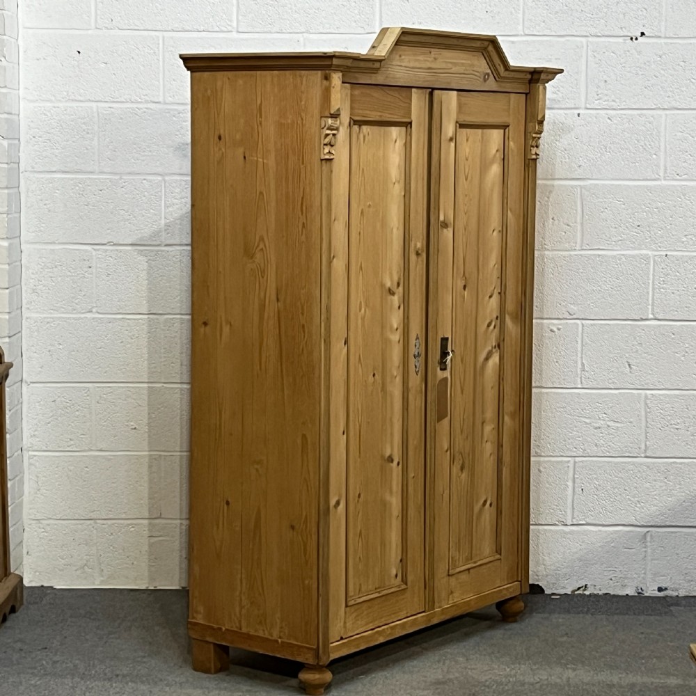 A tall Victorian pine two-door cupboard featuring field-panelled doors, turned bun feet, and a shaped bonnet top pediment. View III