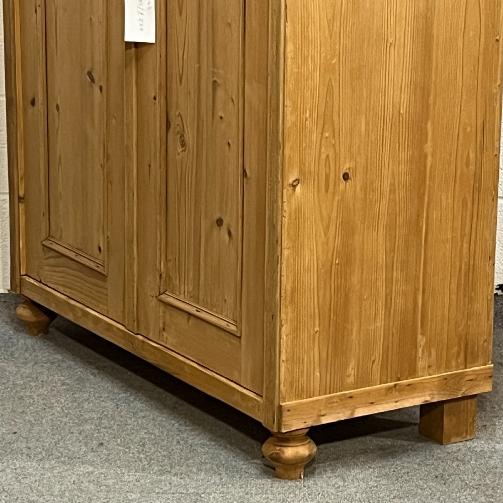 A tall Victorian pine two-door cupboard featuring field-panelled doors, turned bun feet, and a shaped bonnet top pediment. View V