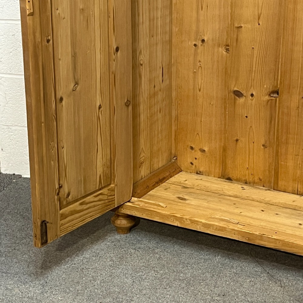A tall Victorian pine two-door cupboard featuring field-panelled doors, turned bun feet, and a shaped bonnet top pediment. View VII