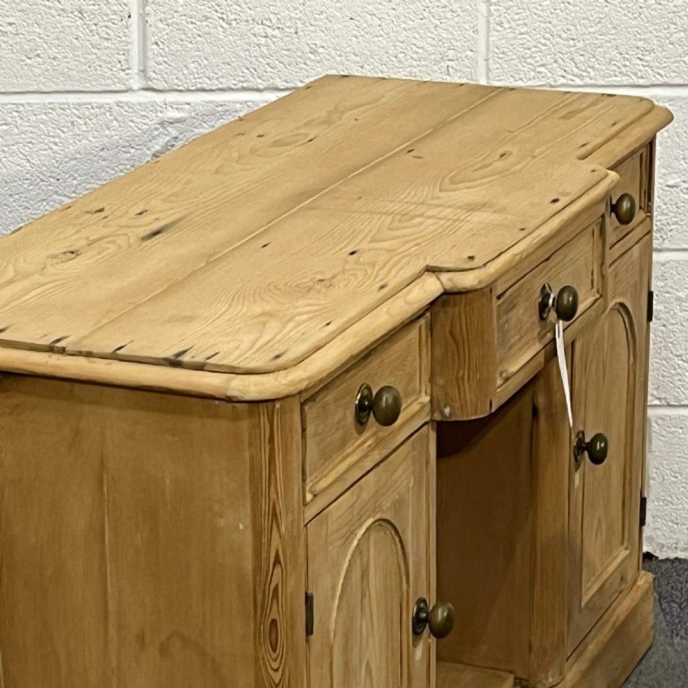 A Victorian pine kneehole writing desk featuring three upper drawers, two arched cupboard doors, metal knobs, and a solid plinth base. View IV