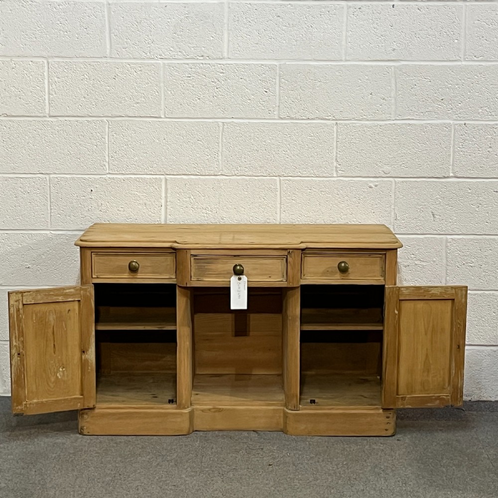 A Victorian pine kneehole writing desk featuring three upper drawers, two arched cupboard doors, metal knobs, and a solid plinth base. View VI