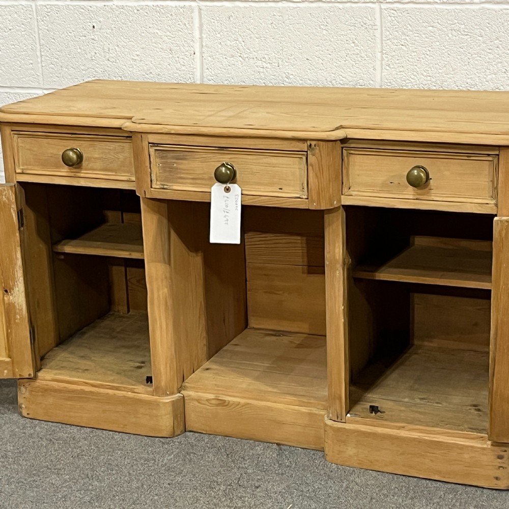 A Victorian pine kneehole writing desk featuring three upper drawers, two arched cupboard doors, metal knobs, and a solid plinth base. View VII