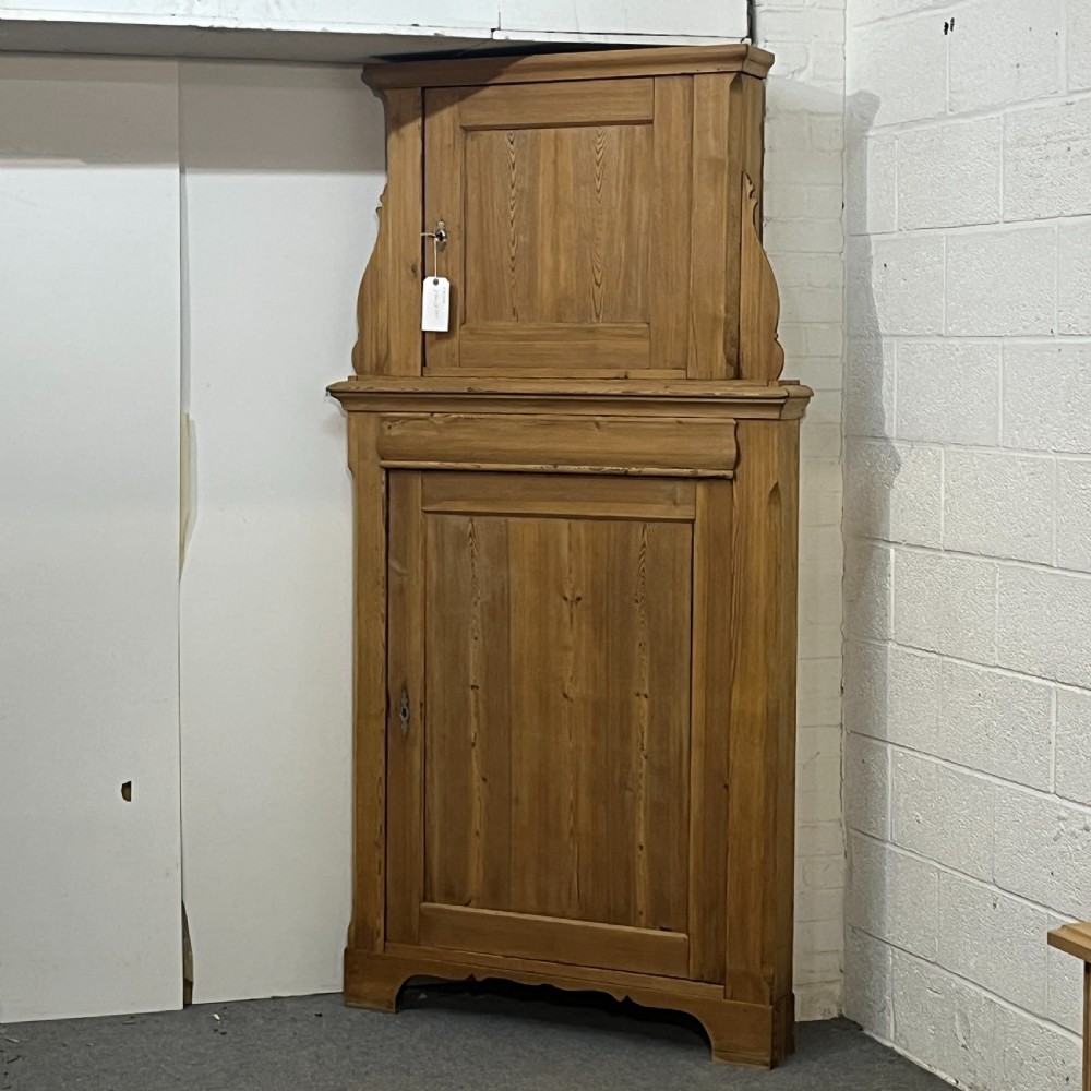 A tall two-tier antique pine corner cupboard with single panelled upper and lower doors and side scroll details. View II