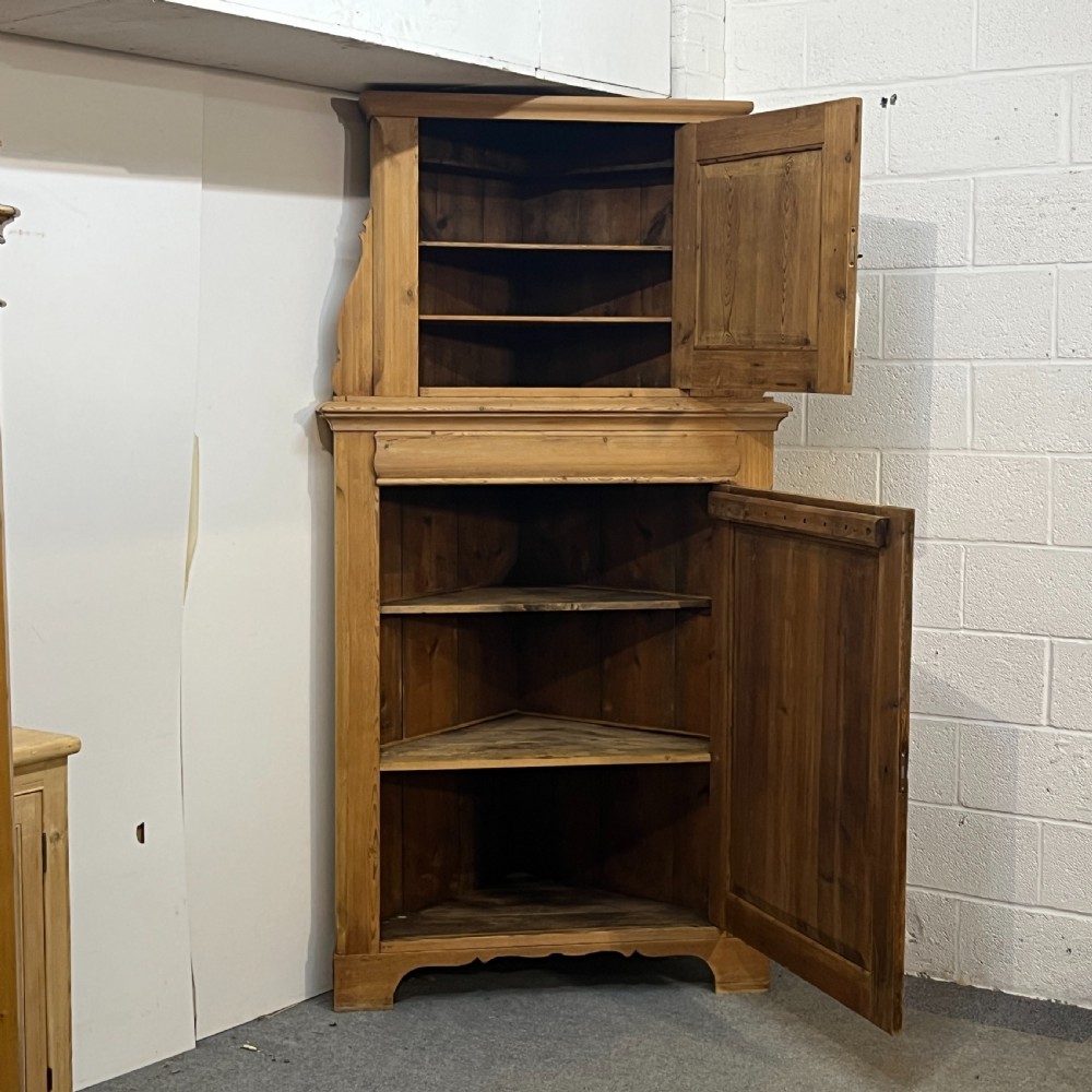 A tall two-tier antique pine corner cupboard with single panelled upper and lower doors and side scroll details. View III