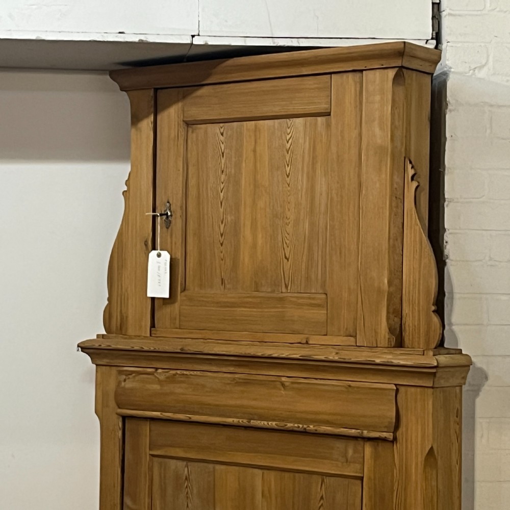A tall two-tier antique pine corner cupboard with single panelled upper and lower doors and side scroll details. View V