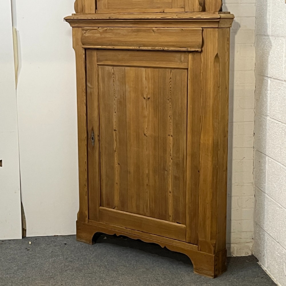 A tall two-tier antique pine corner cupboard with single panelled upper and lower doors and side scroll details. View VI