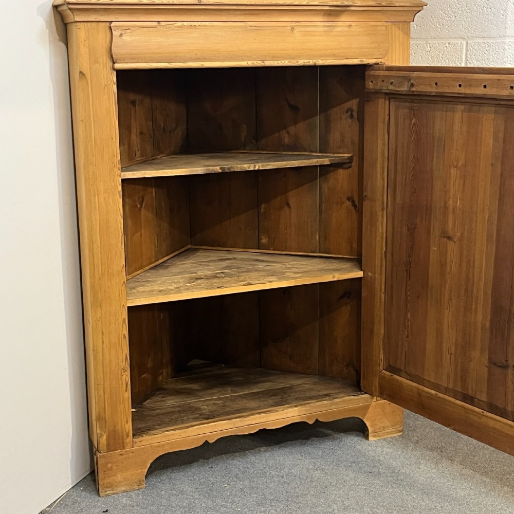 A tall two-tier antique pine corner cupboard with single panelled upper and lower doors and side scroll details. View VII