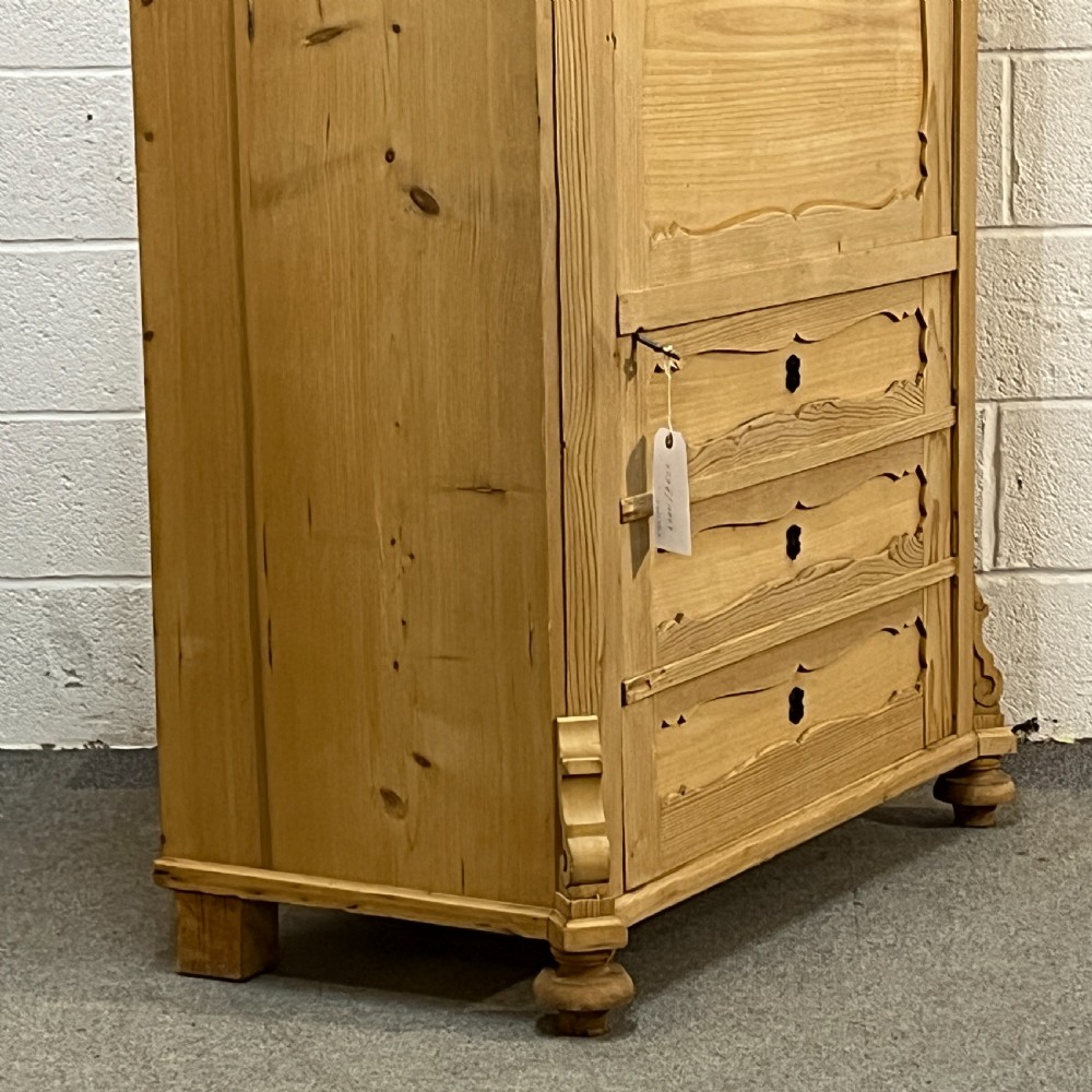 A tall antique pine single-door cupboard featuring a decorative carved cresting, moulding styled like drawers, central keyholes, and turned feet. View VII