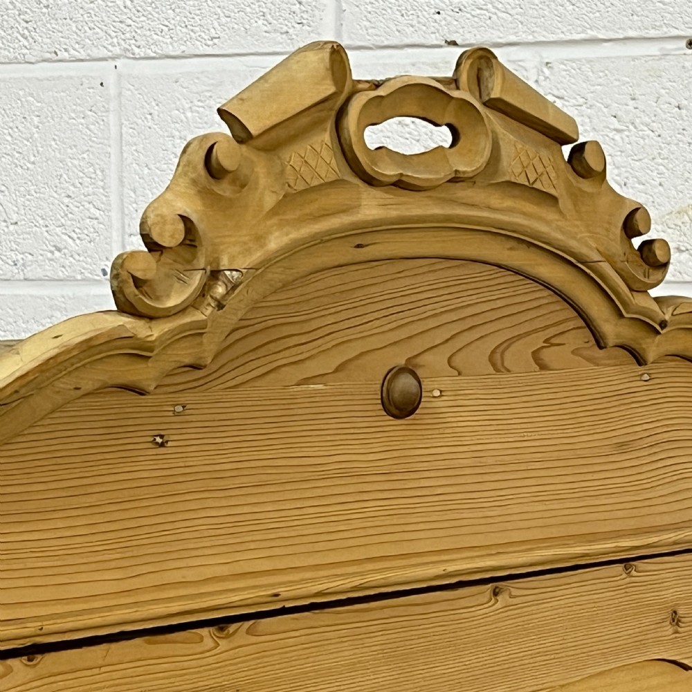 A tall antique pine single-door cupboard featuring a decorative carved cresting, moulding styled like drawers, central keyholes, and turned feet. View VIII