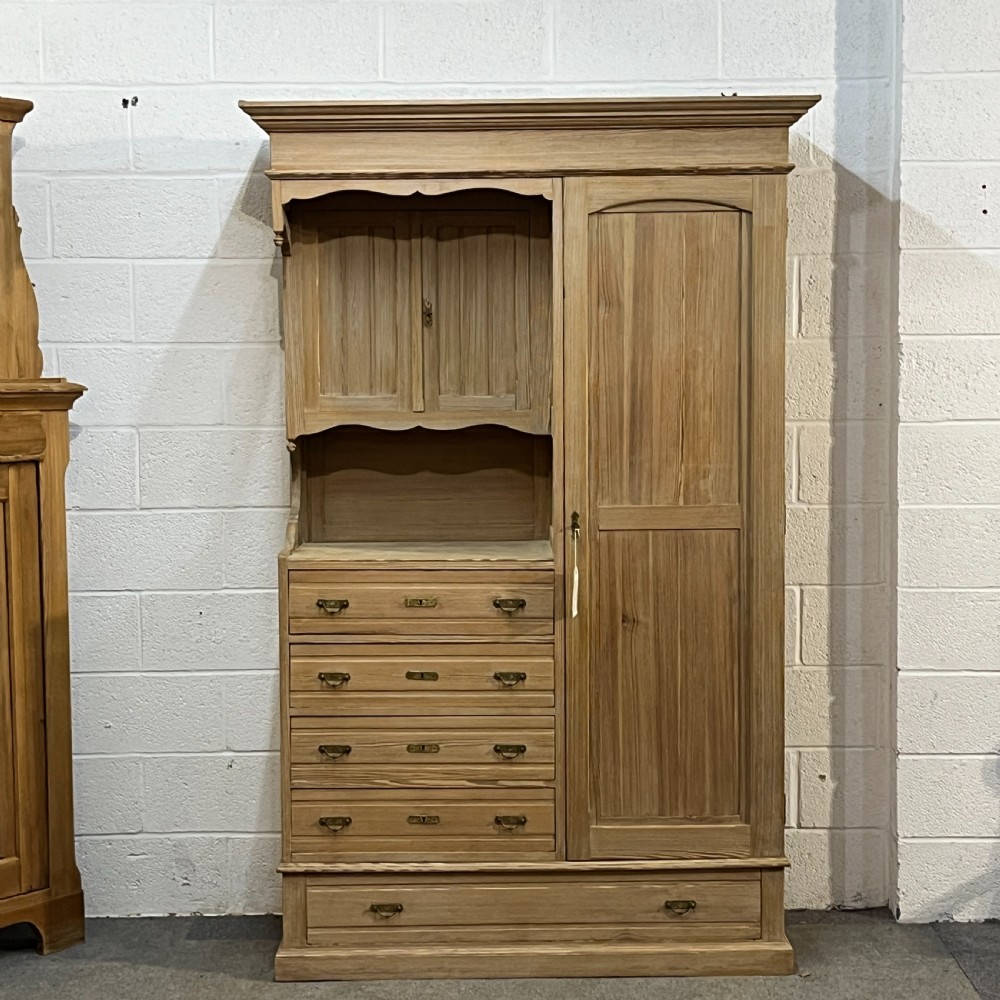 A tall antique stripped pine combination cupboard unit featuring a single long door, upper cabinet, open alcove, side drawers, and a base drawer.
