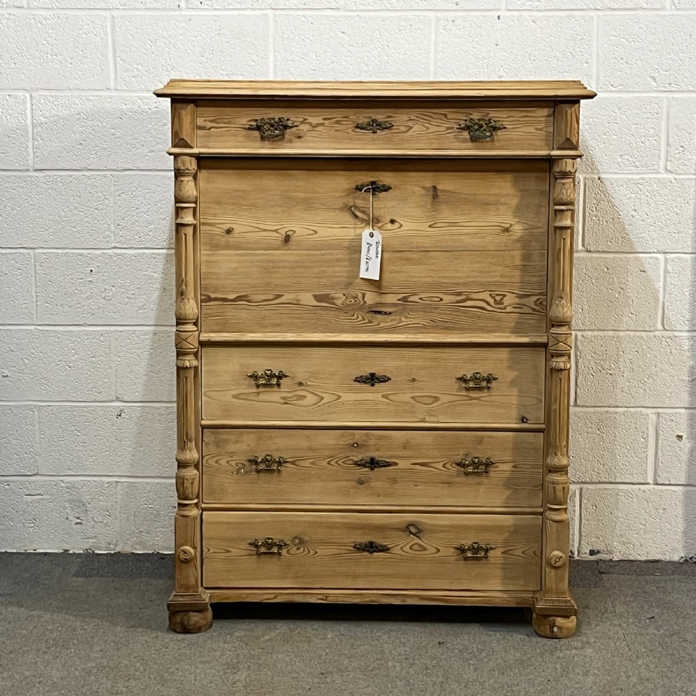 An antique pine secretaire desk featuring a fall-front writing compartment above multiple drawers, decorated with turned side columns and dark metal handles. View II